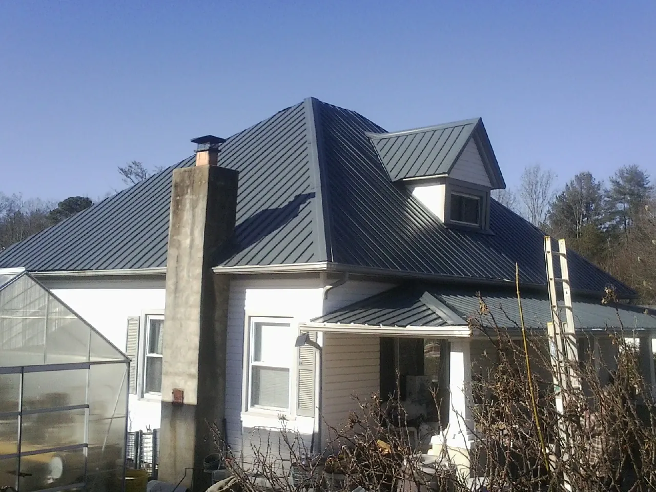 Dark blue standing seam metal roof on a white farmhouse with dormer — Slate & Tile Roof Repair by Roofing Brothers in Schertz
