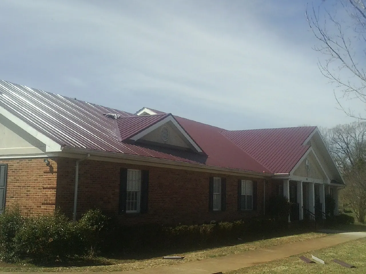 Red metal roof with gabled entries on a long brick building, from a Hail Damage Roof Repair job in Schertz