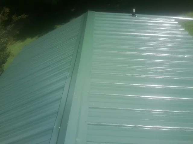 New green metal panels meeting at the ridge of a roof — Flat Roof Repair work by our crew in Schertz