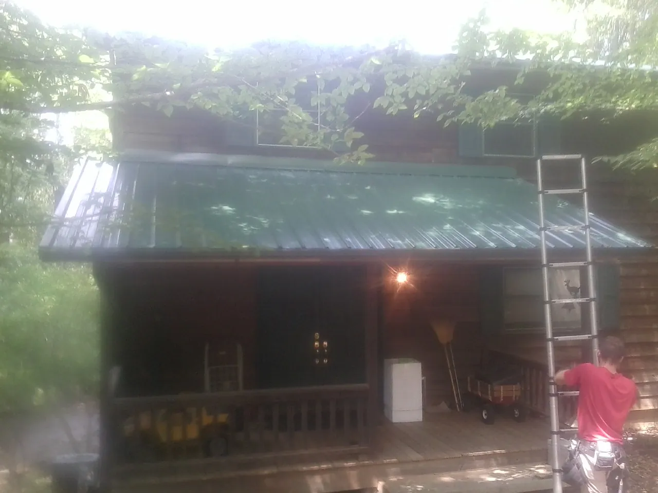 Worker on a ladder at the green porch roof of a wooded cabin in Schertz