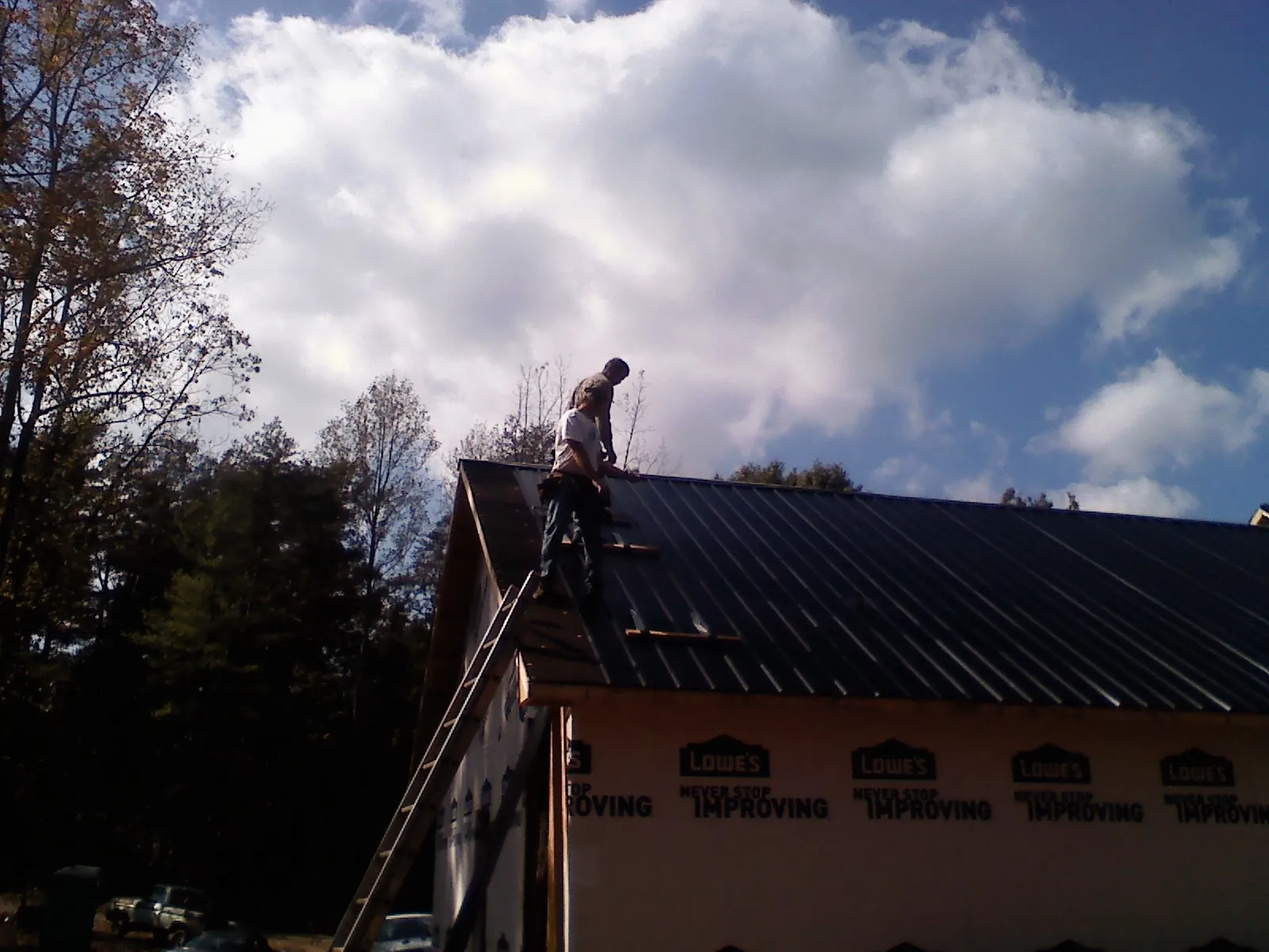 Roofer fastening dark metal panels high against a cloudy sky, from a Roof Inspection job in Schertz
